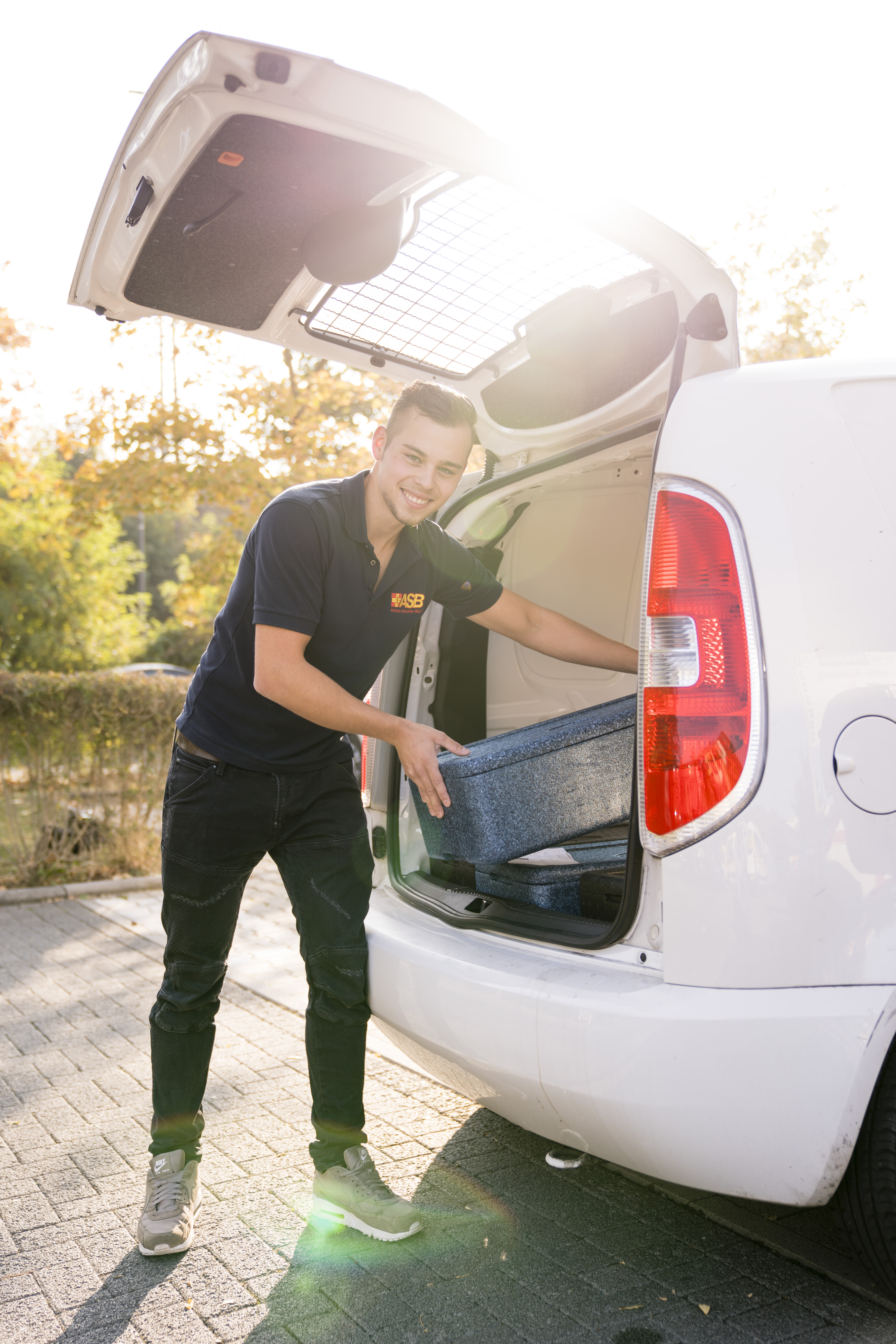Ein junger Mann begleitet lädt eine Kiste in ein Fahrzeug ein.
