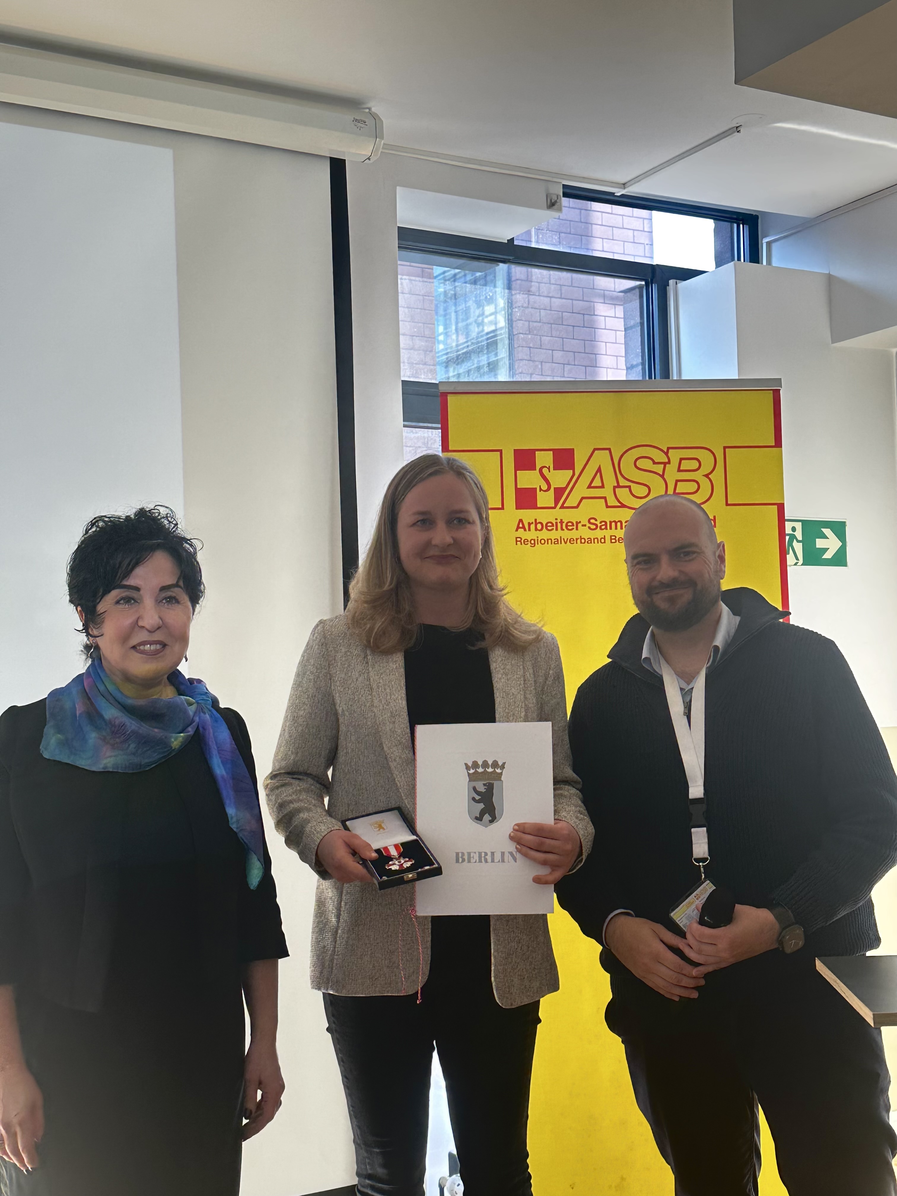 Bezirksbürgermeisterin Emine Demirbüken-Wegner mit Antonia Wieschollek, die für zehn Jahre aktive Mitarbeit im Katastrophenschutz das Feuerwehr- und Katastrophenschutz-Ehrenzeichen in Silber erhielt,  und Daniel Ullrich, scheidender Vorsitzender des ASB-Regionalverbands. Dessen Nachfolge tritt Sven Beutner an.